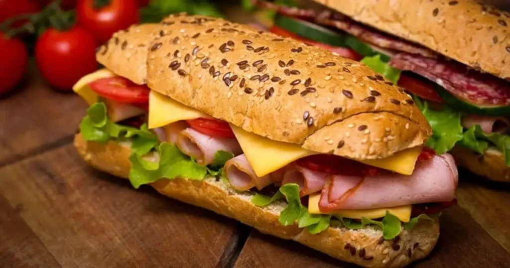 Two 6 inches long sub sandwiches filled with meat, cheese, and tomatoes, presented on a clean white plate.