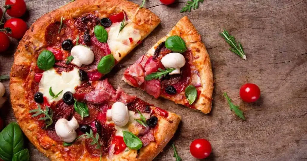  A 6 Inches Long Small Pizza Size topped with meat, cheese, and tomatoes, displayed on a rustic wooden table.