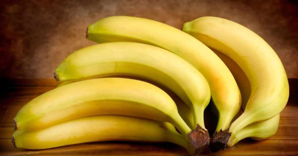 A bunch of bananas, each approximately 8 inches long, resting on a rustic wooden table, showcasing their vibrant yellow color.