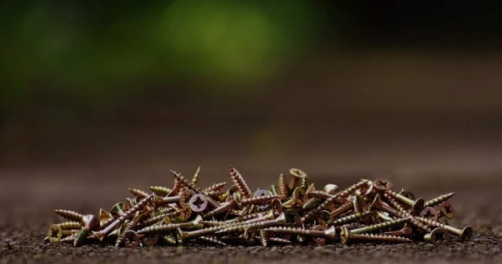  A pile of 2mm screws scattered on a wooden floor, showcasing their metallic sheen against the natural wood grain.